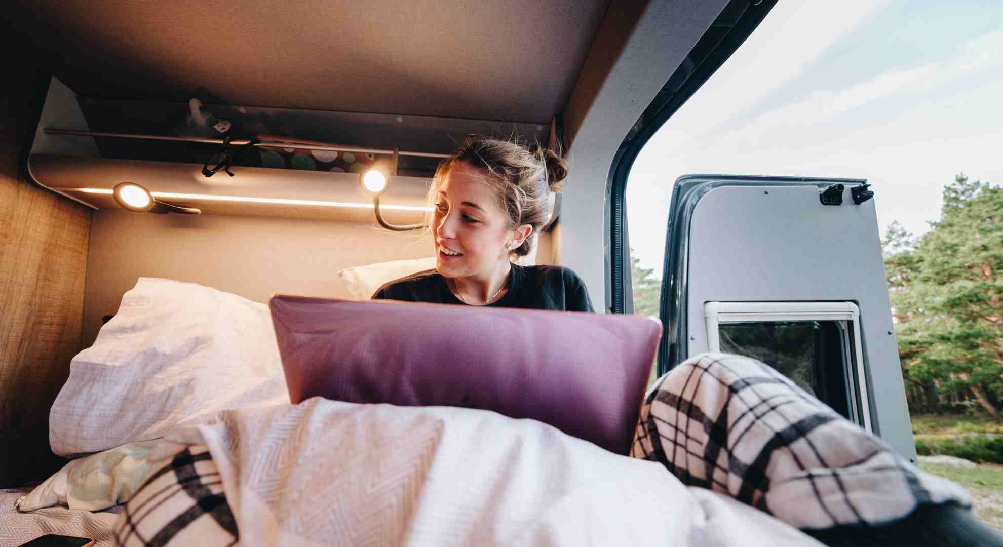 Mlada ženska dela na prenosniku v avtodomu in uživa v razgledu skozi okno.